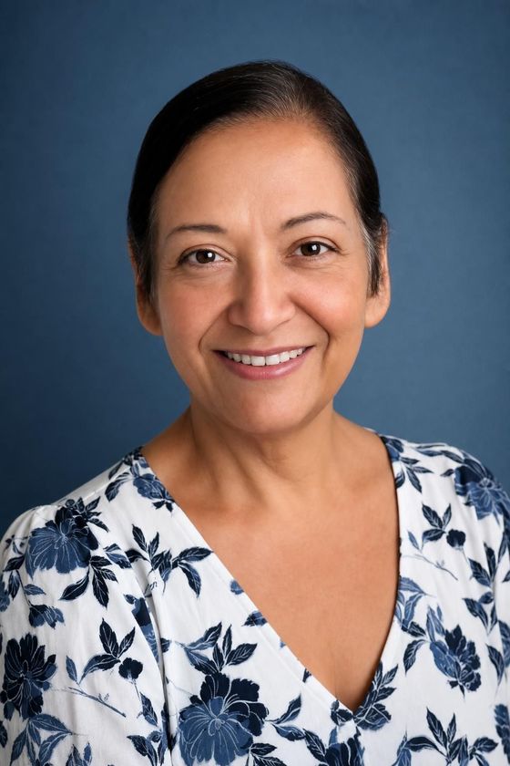 Smiling woman in a white floral blouse against a blue studio backdrop
