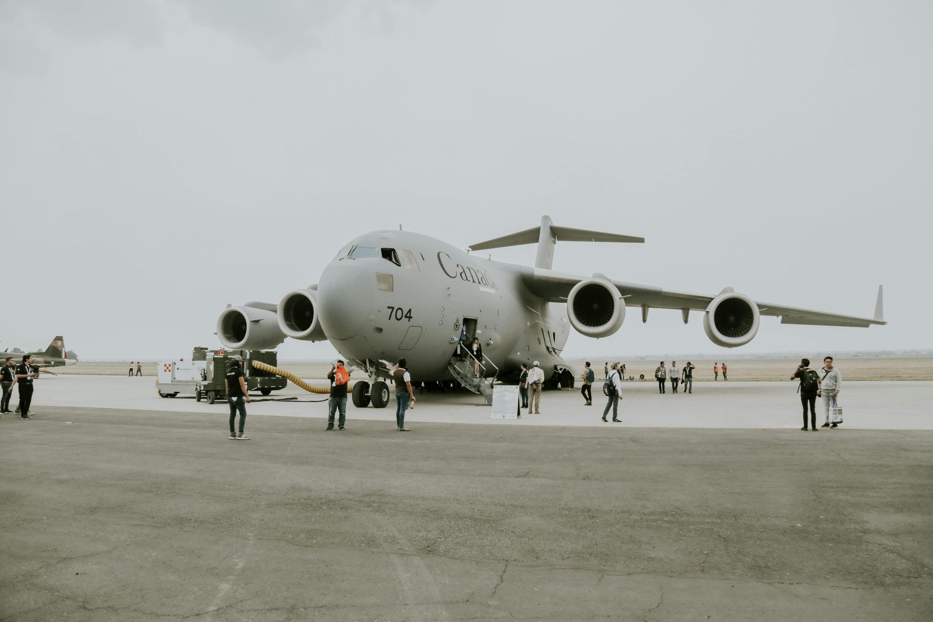Large gray cargo plane on a runway with several people standing nearby under an overcast sky