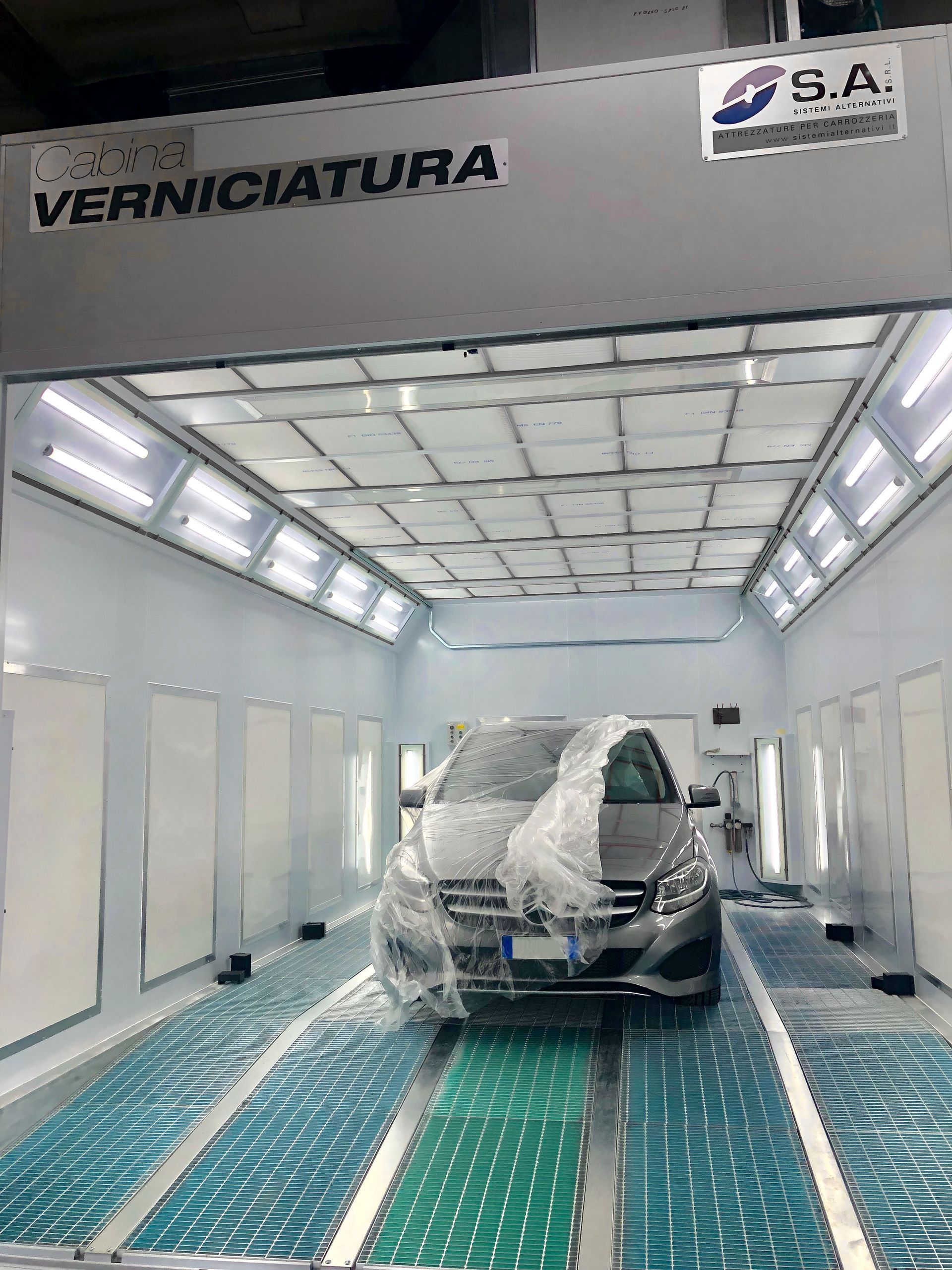 Un'auto è parcheggiata all'interno di una cabina di verniciatura ricoperta di plastica.