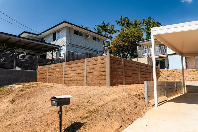 Brick retaining wall on a sloped yard beside a driveway and house under a bright blue sky