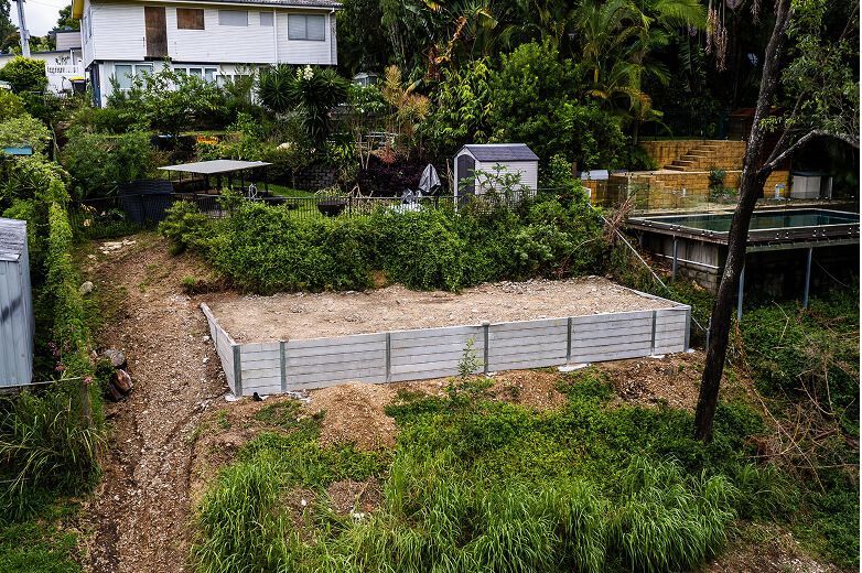 Raised garden bed in a lush backyard with a house and trees in the background
