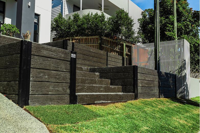 Black tiered retaining wall beside green lawn and white house exterior stairs