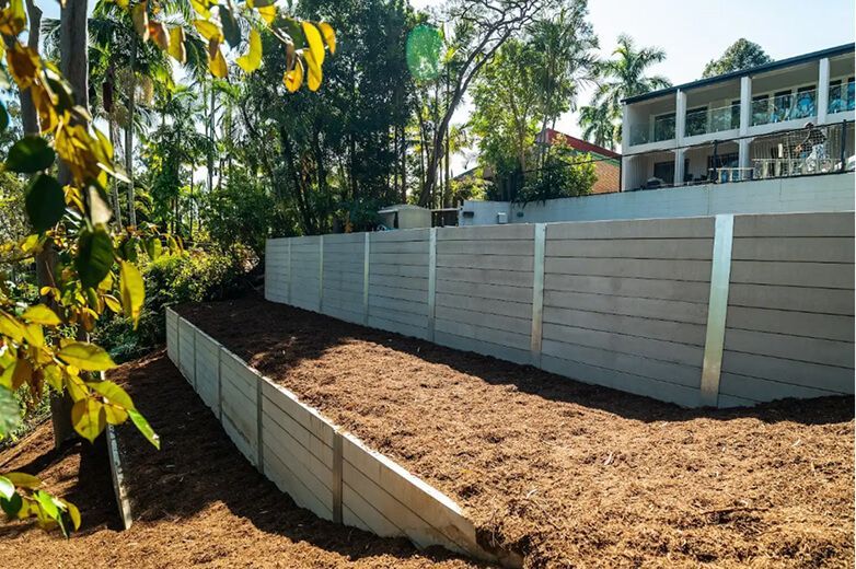 Long white retaining wall beside a mulched garden bed, with trees and a building in the background
