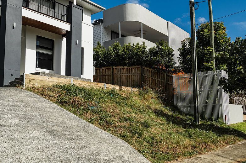 Modern house on a sloped front yard with driveway, fence, and blue sky