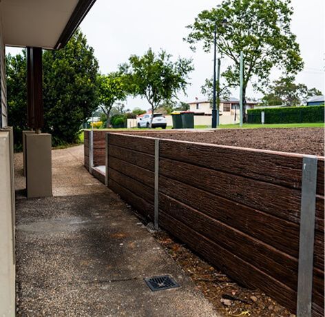 Covered outdoor walkway beside a brown privacy fence, overlooking a grassy park and trees.