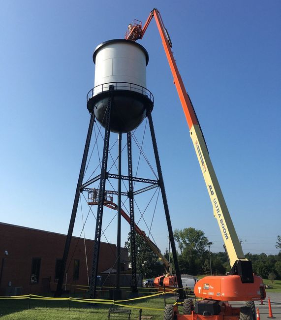 Crane lifting a large white water tower onto a steel frame at an outdoor construction site