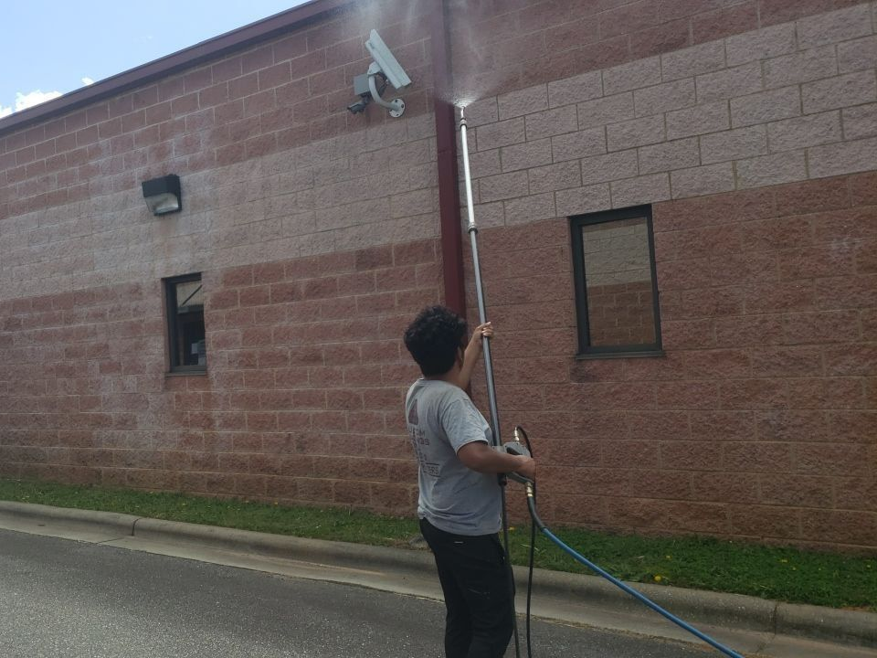 Person using a long pole to inspect a brick building wall outdoors