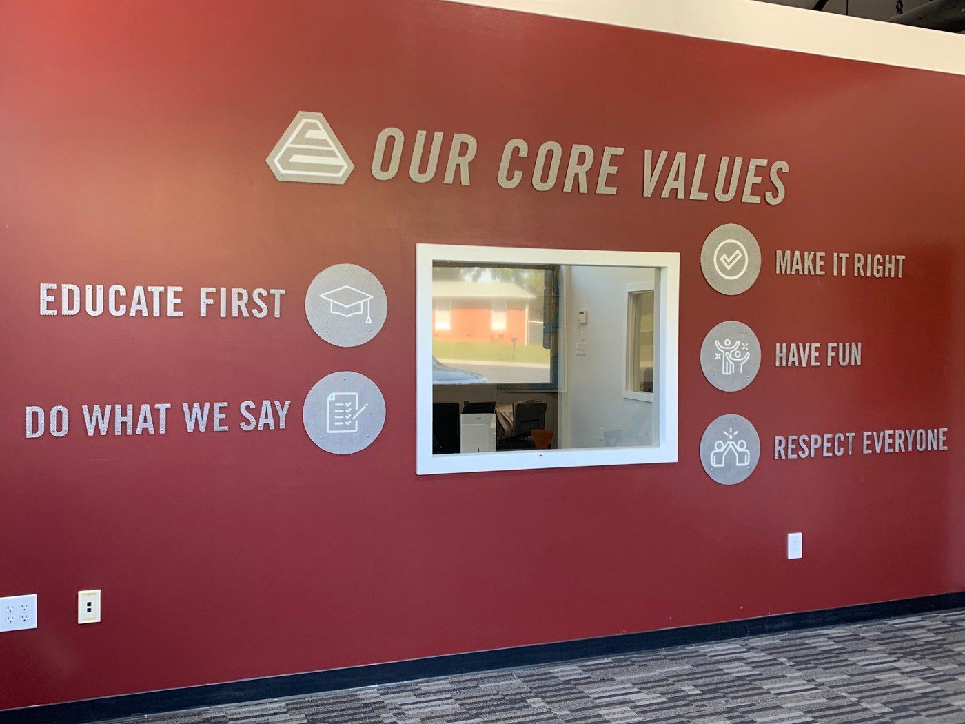 Red wall with “Our Core Values” signs, motivational text, and a small window opening