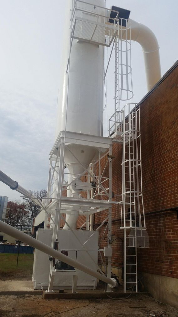 Tall white industrial ducting and metal tower beside a brick building with ladders and pipes