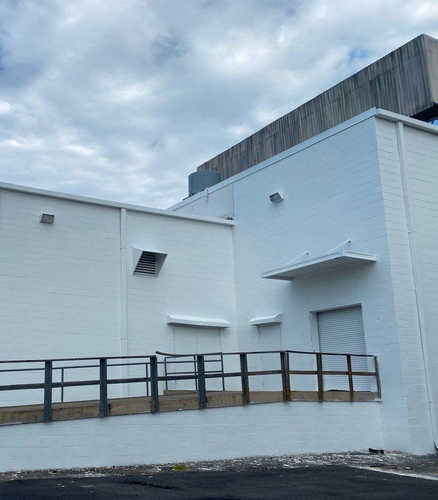 White brick building with ramp railing and small awnings under a cloudy sky