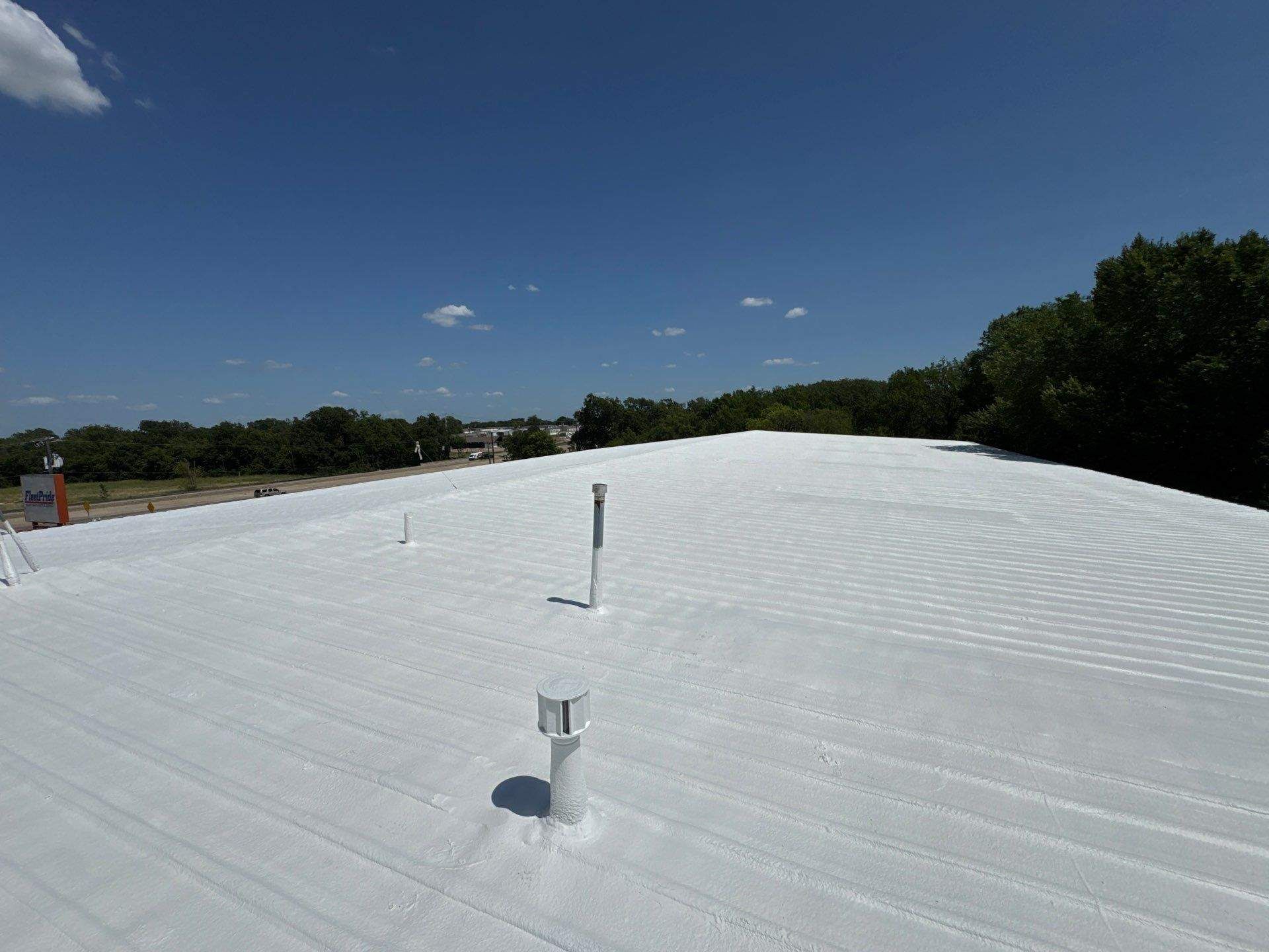 White rooftop with vents under a clear blue sky, bordered by trees.
