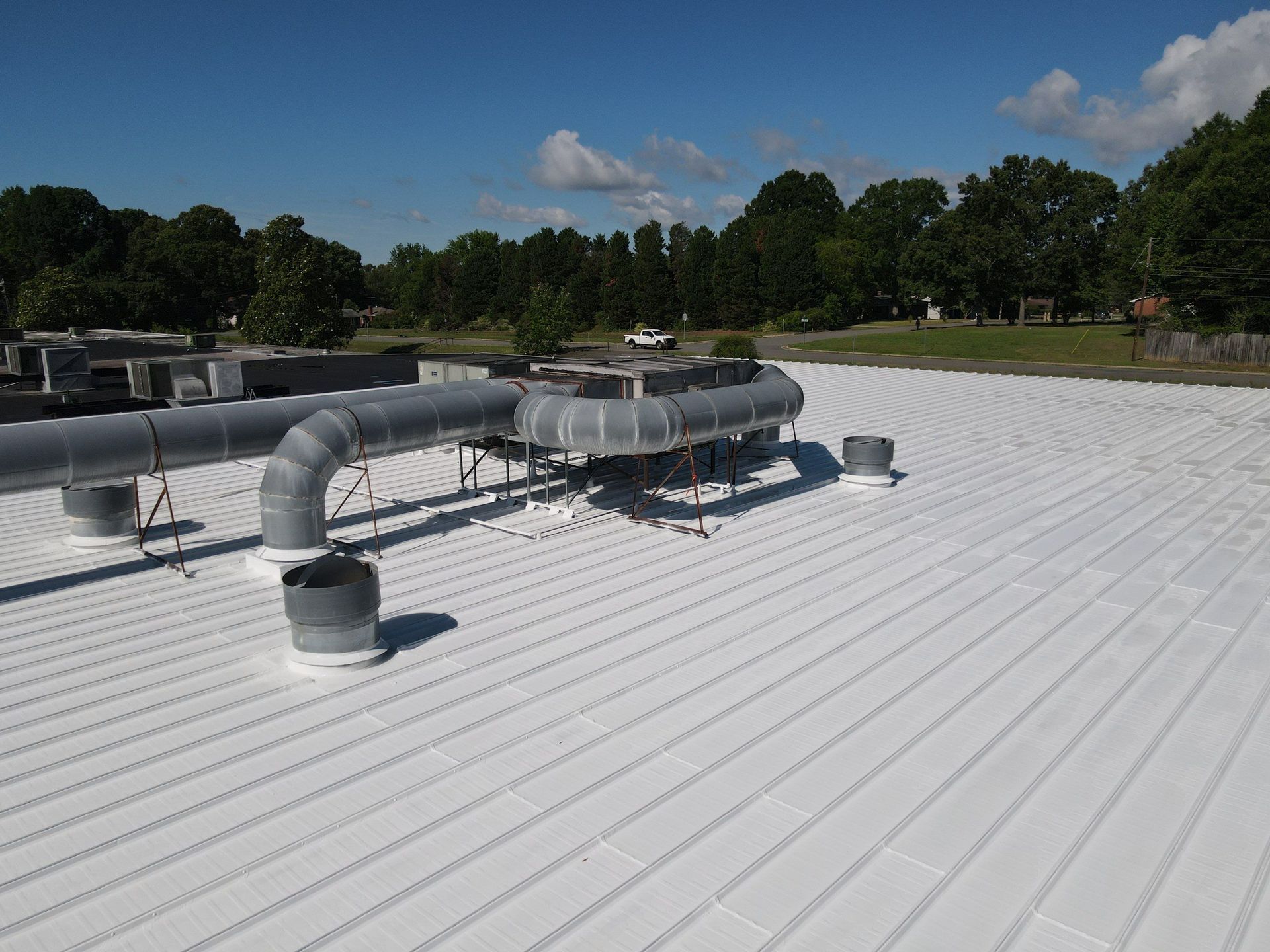 Rooftop HVAC equipment on a white metal roof under a blue sky, with trees in the background