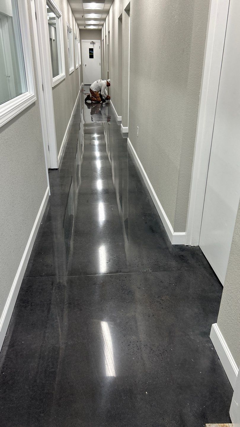 Person kneeling in a narrow hallway with glossy dark floor and white walls.