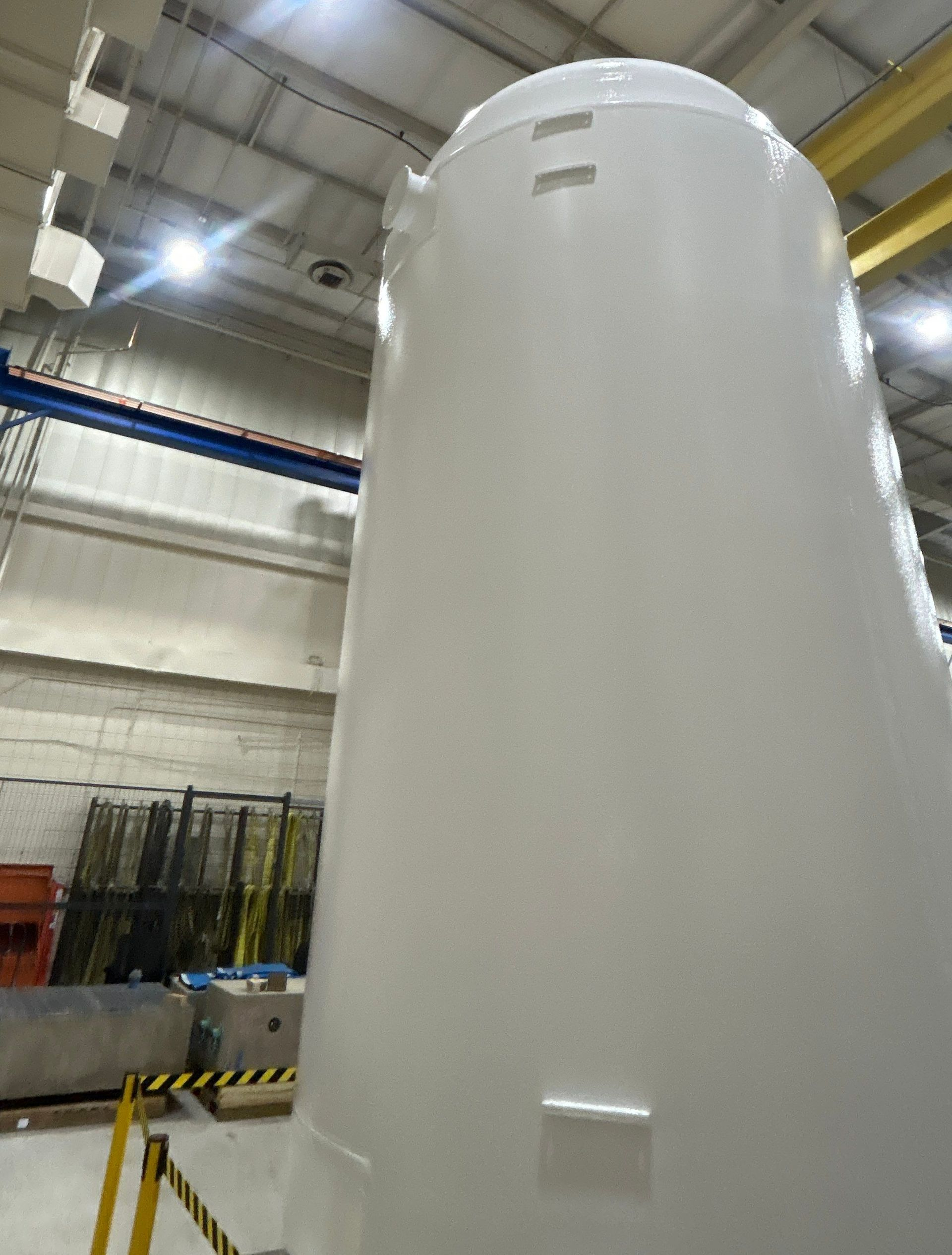 Large white industrial tank inside a factory, with overhead beams and lighting.