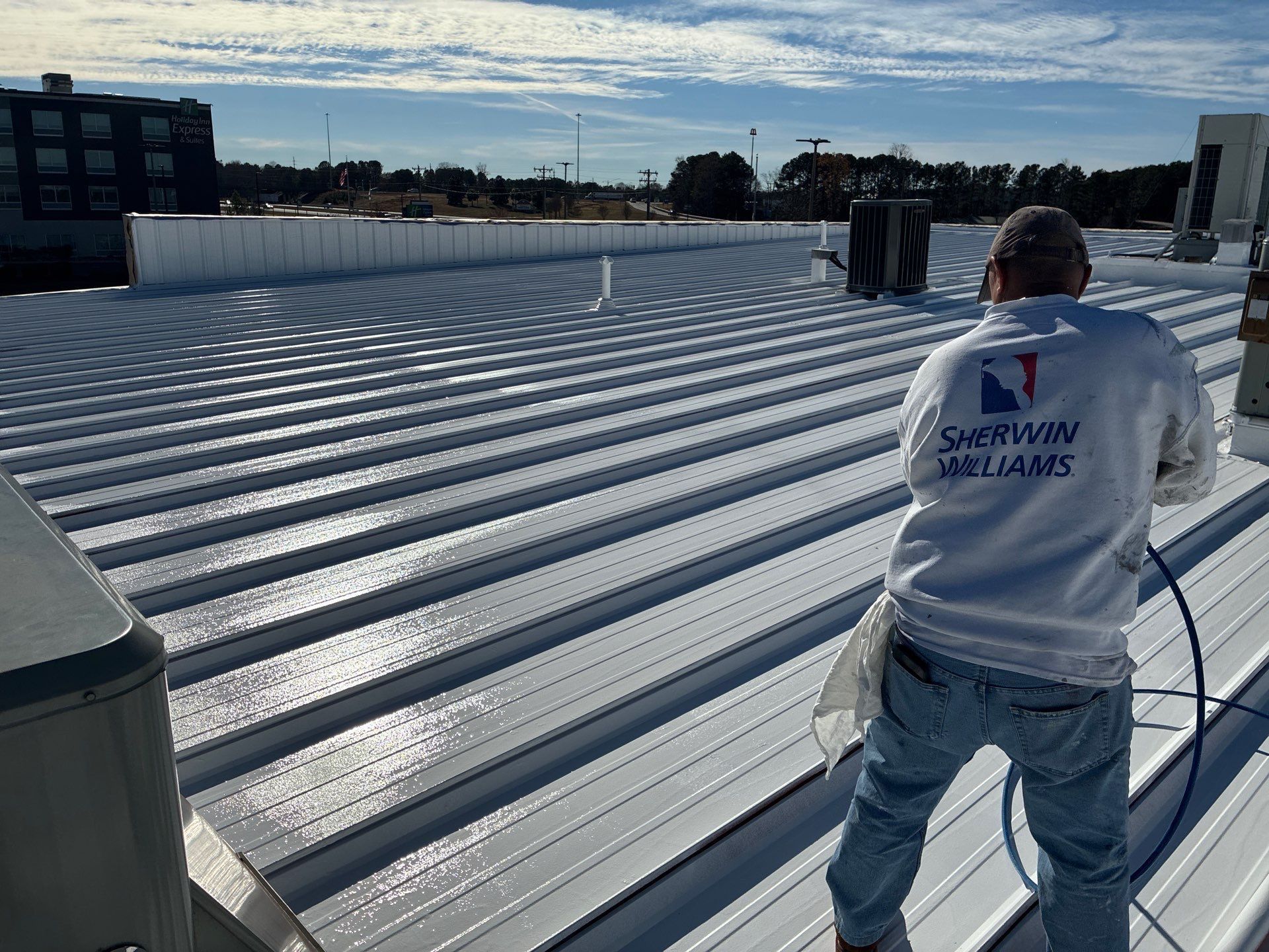 Worker on a corrugated metal rooftop under a blue sky, preparing for roofing work.