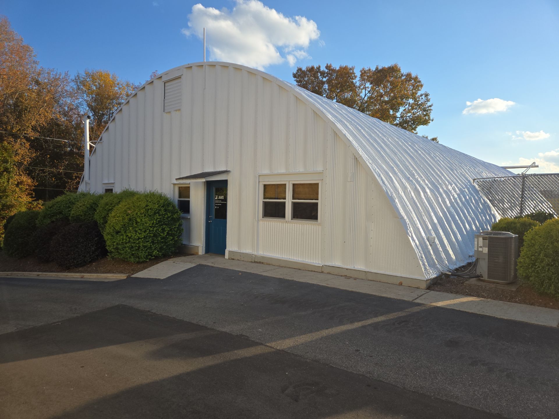White arched building with a blue door and windows, viewed from a parking lot on a sunny day.
