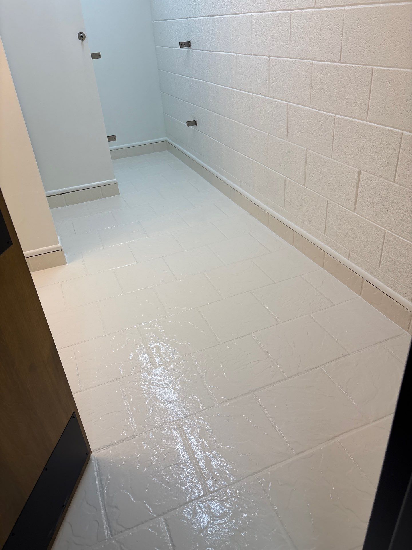 Narrow white-tiled hallway with glossy wet floor and cinderblock wall.