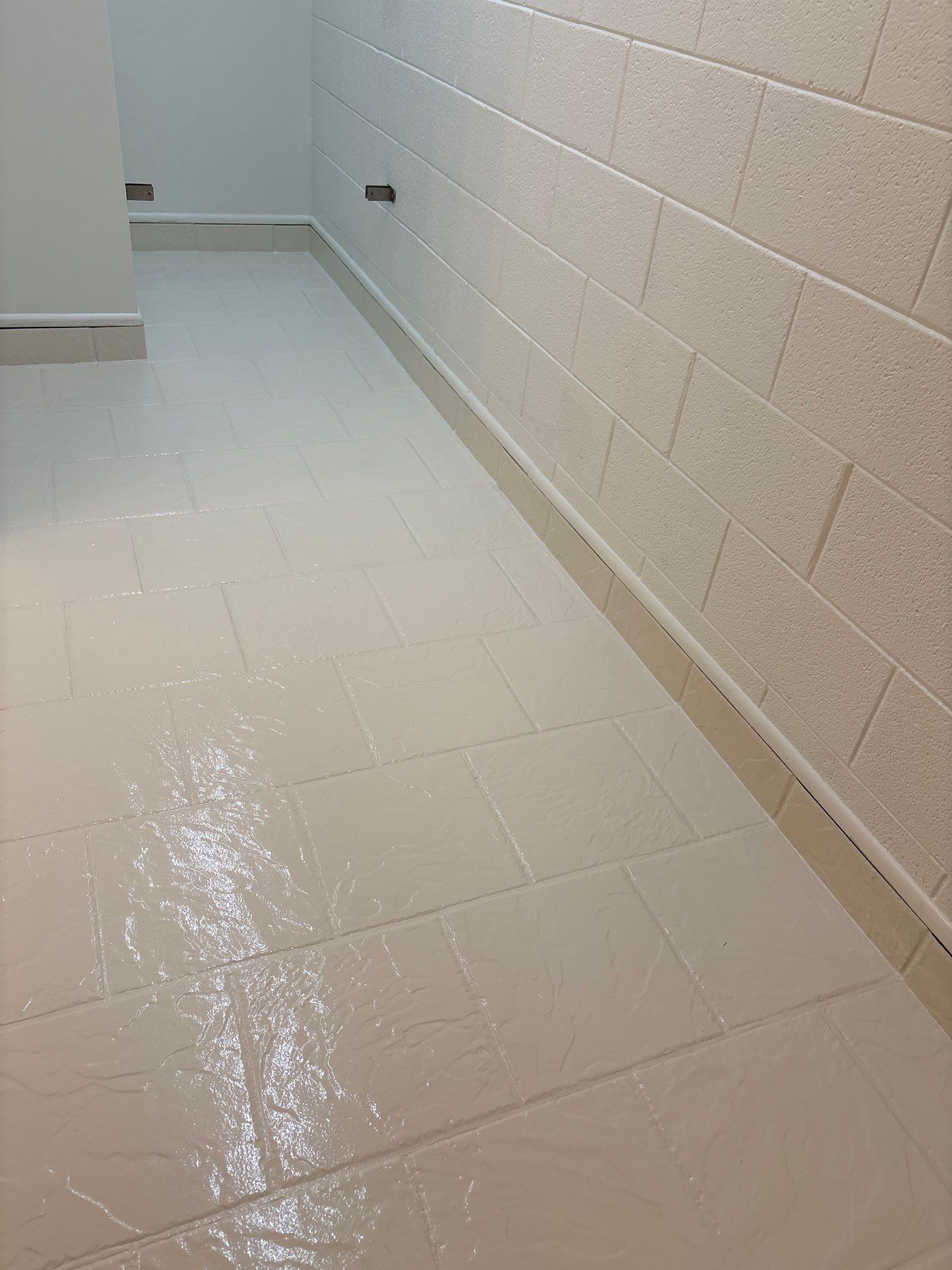 Wet white tiled hallway with cinderblock walls and a floor drain