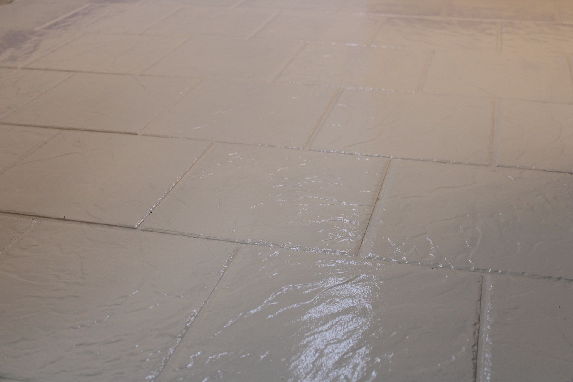 Wet beige tiled floor with reflective puddles and grout lines.