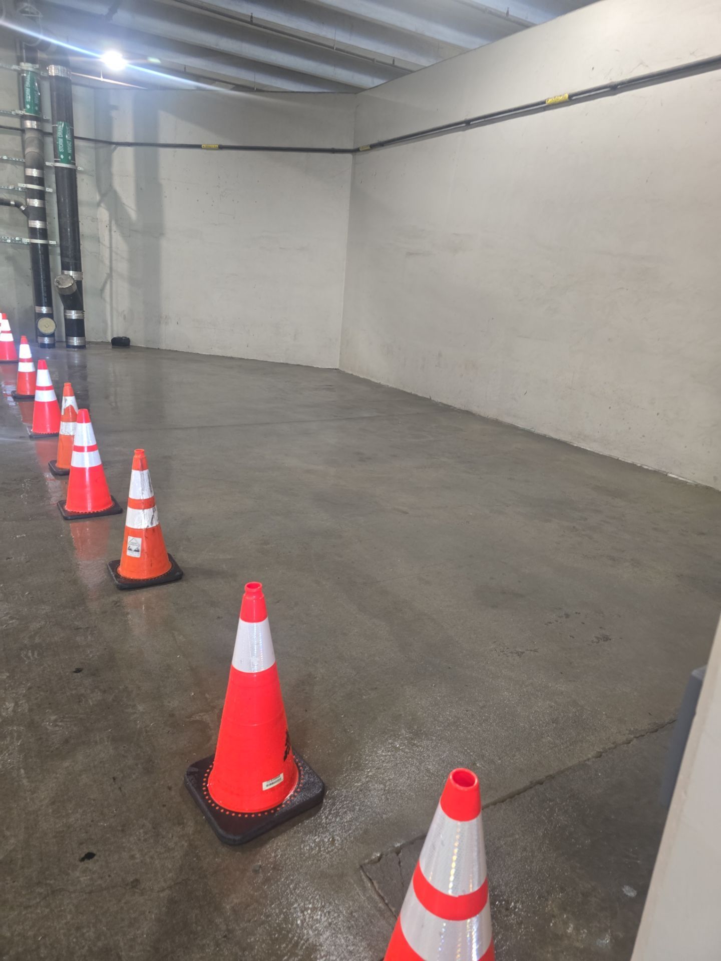 Indoor concrete corridor lined with orange traffic cones and a white wall