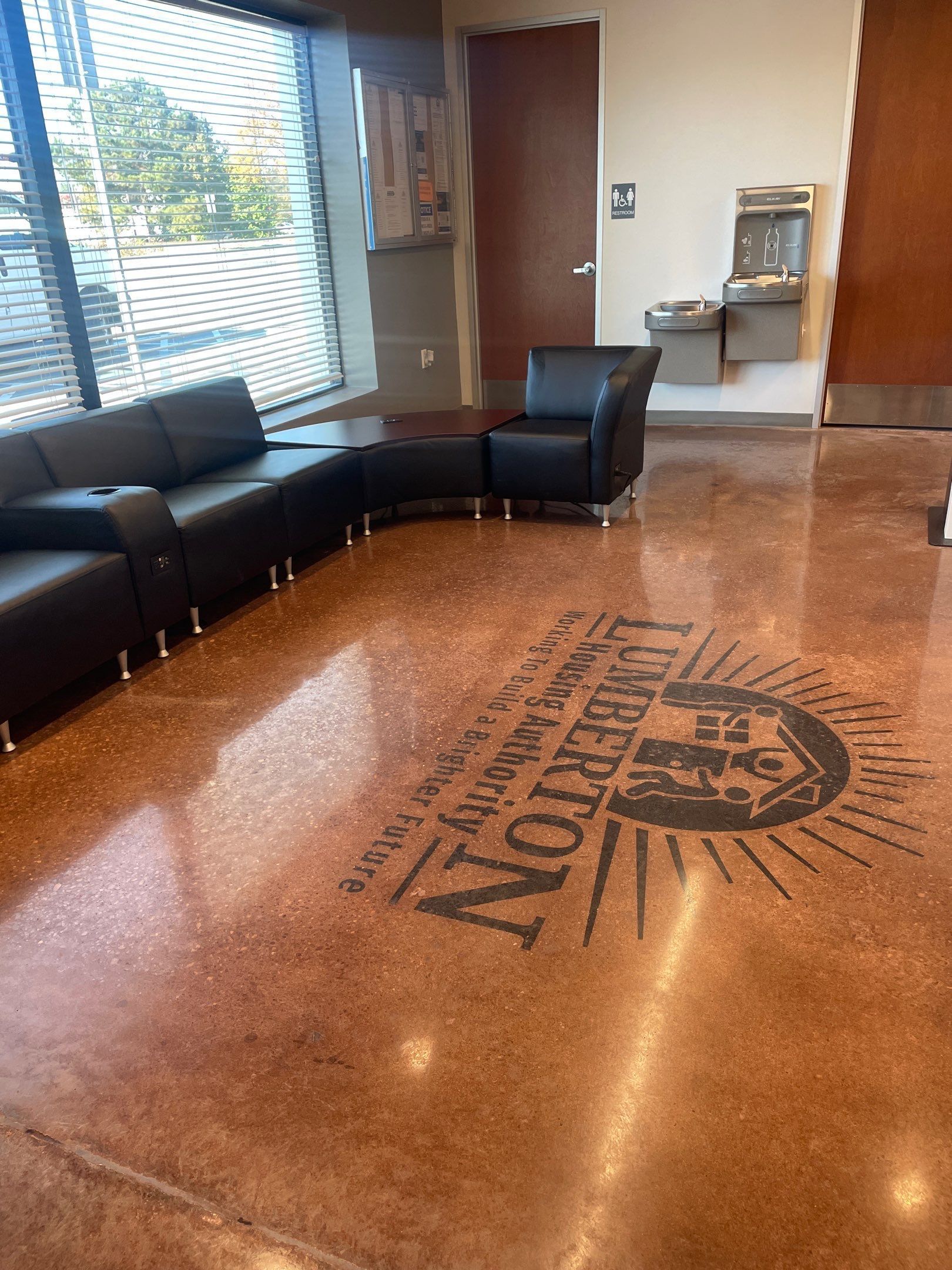 Lobby with black leather chairs, glossy tiled floor, and a large sun logo in the center.