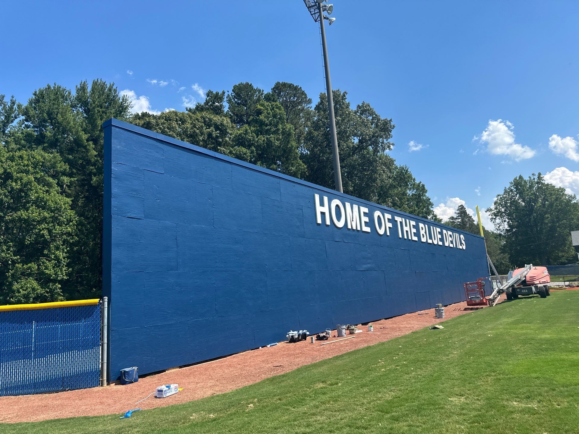 Blue wall with white “HOME OF THE BULLDOGS” lettering beside a grassy field under a bright sky