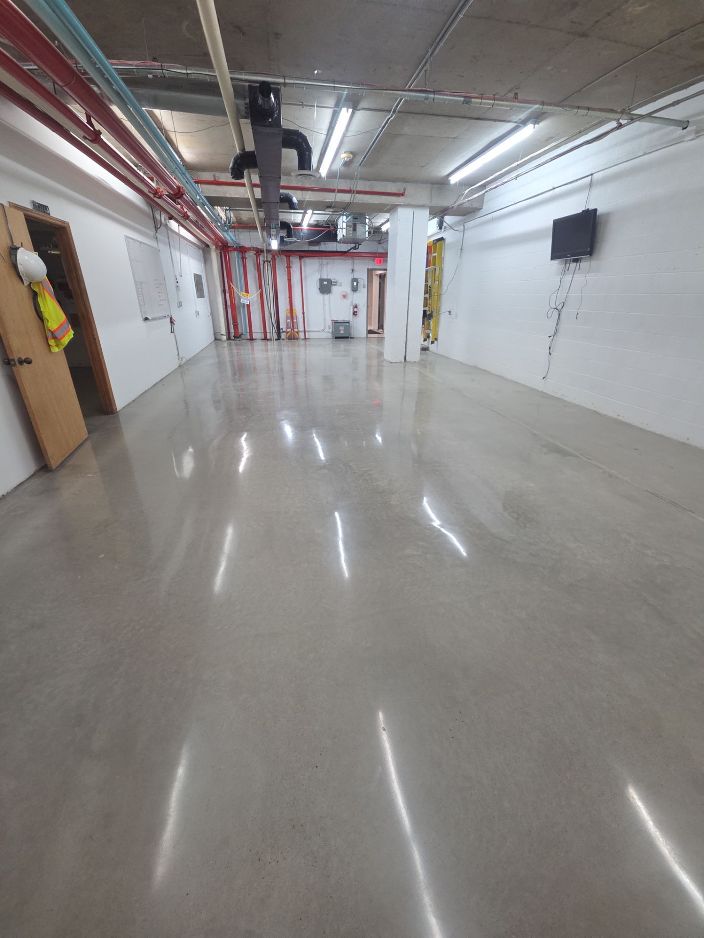 Empty underground hallway with polished concrete floor, white walls, and exposed pipes overhead