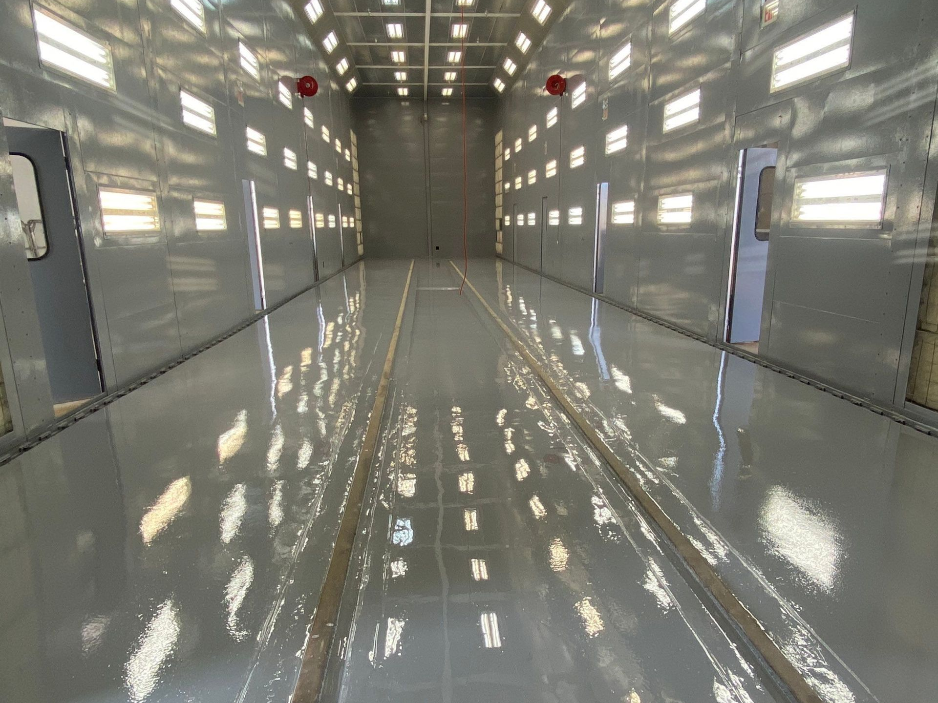 Bright empty industrial hallway with glossy white walls and reflections, lit by overhead lights.