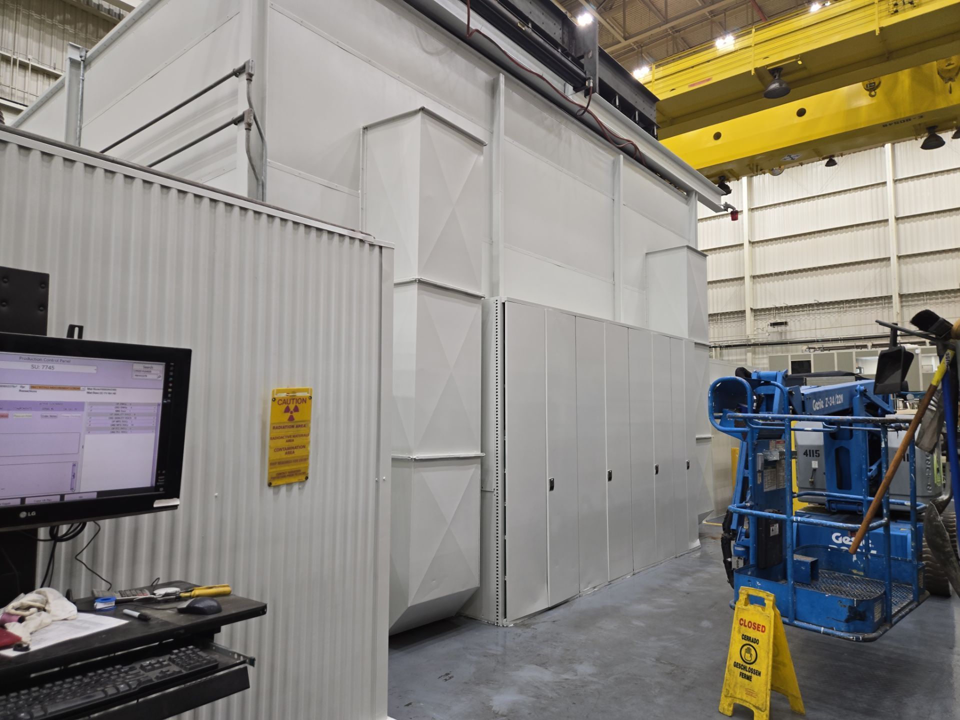 Industrial warehouse interior with white partition walls, blue lift equipment, and a computer monitor on a desk