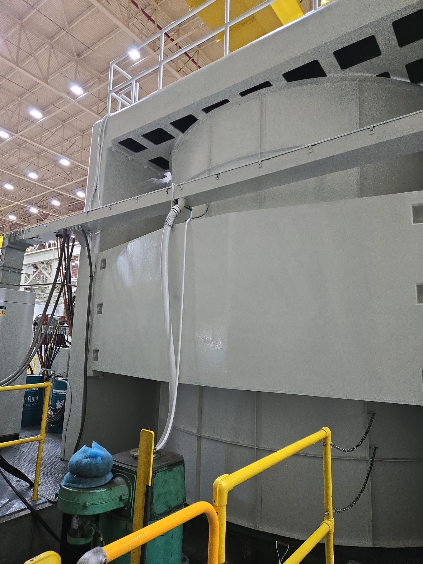 Large industrial machine in a factory, with gray panels, yellow railings, and overhead catwalks.