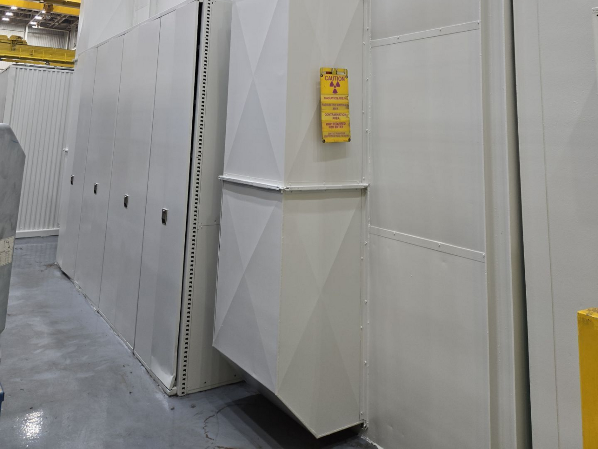 Industrial white equipment cabinets in a factory aisle with a yellow warning sign.
