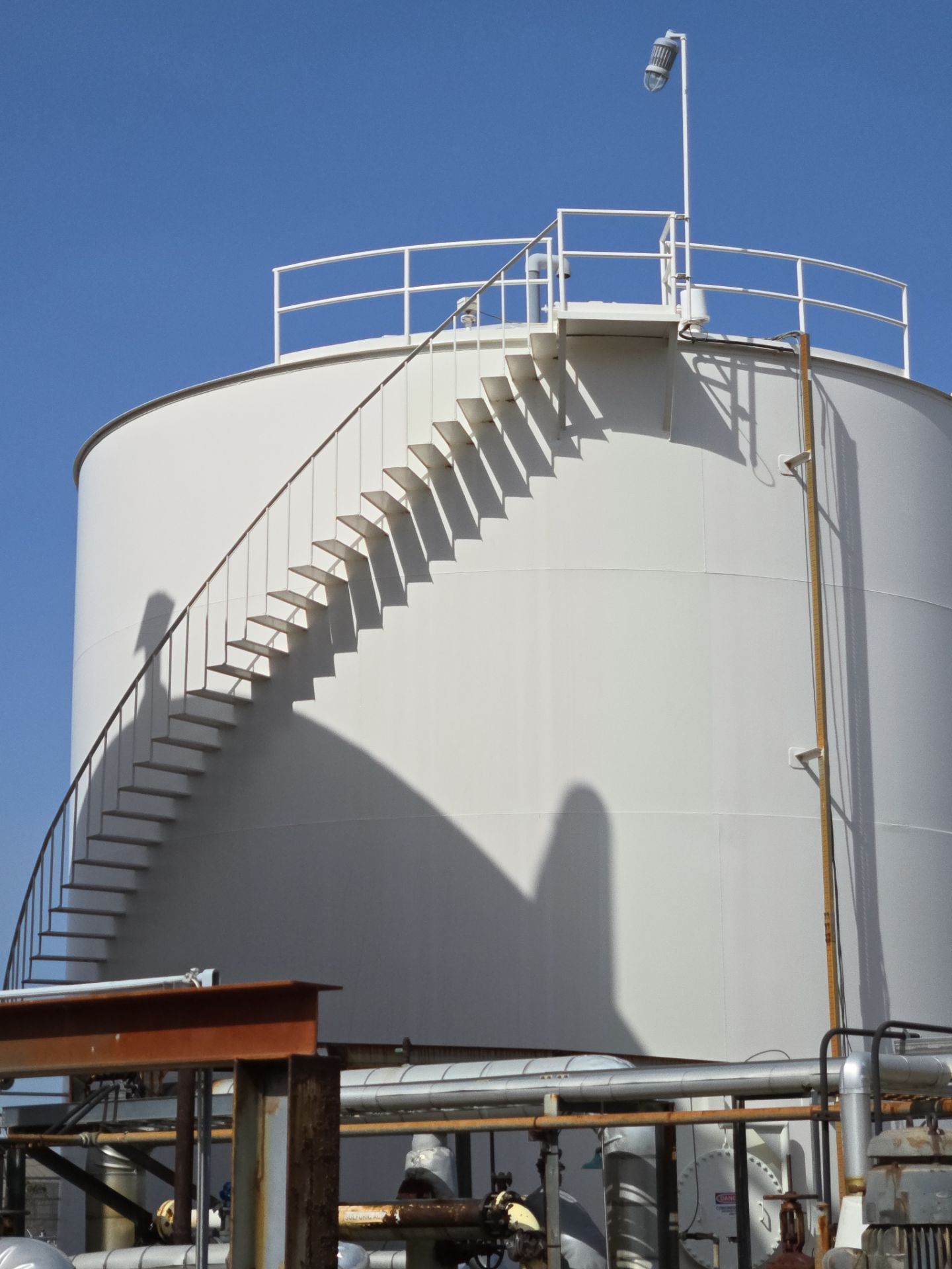 Large white industrial storage tank with stairs and railings against a clear blue sky