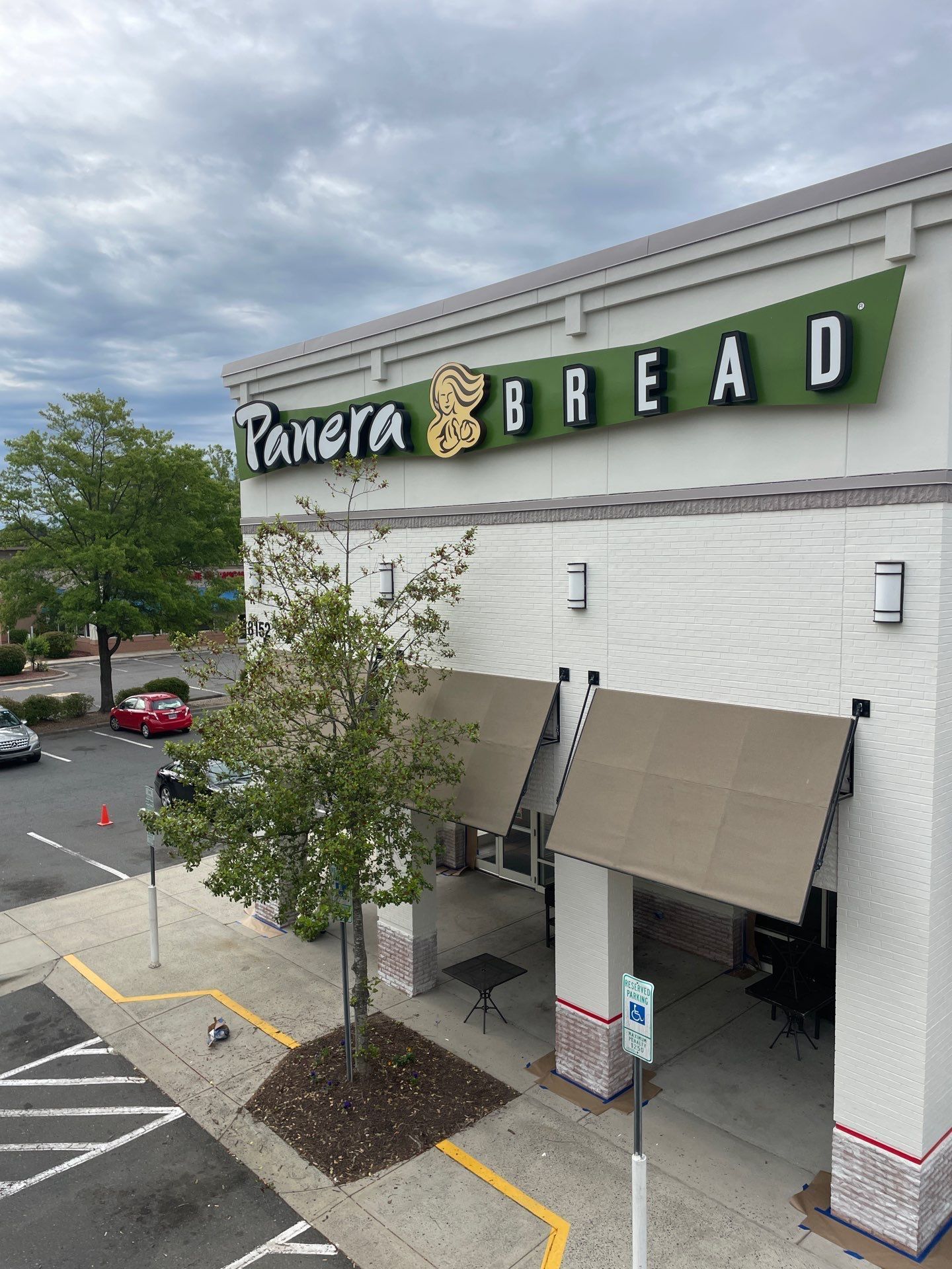 Panera Bread storefront with green sign, awnings, and parking lot outside