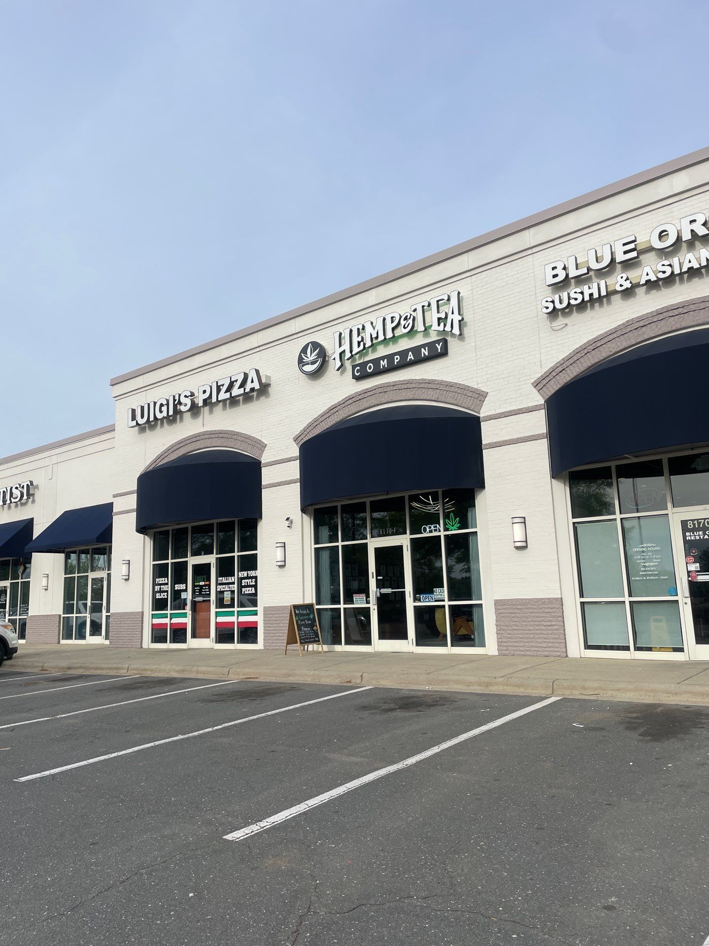 Strip mall storefronts with blue awnings and empty parking spaces under a clear sky