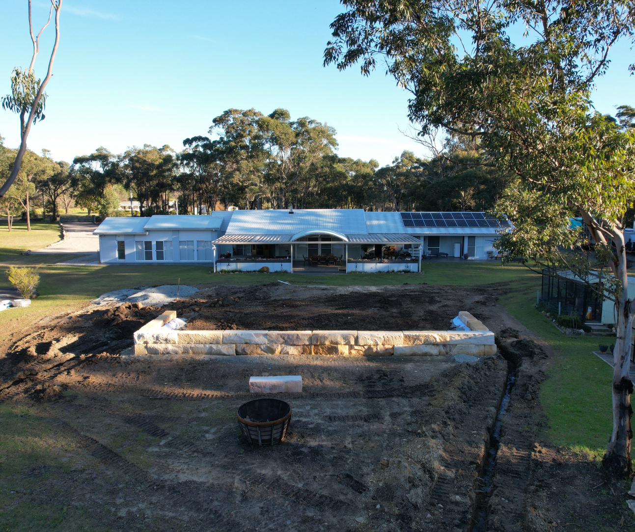 Single-story white house with a metal roof in a wooded yard, with a rectangular concrete foundation in front. Single-story white house with a metal roof in a wooded yard, with a rectangular concrete foundation in front.