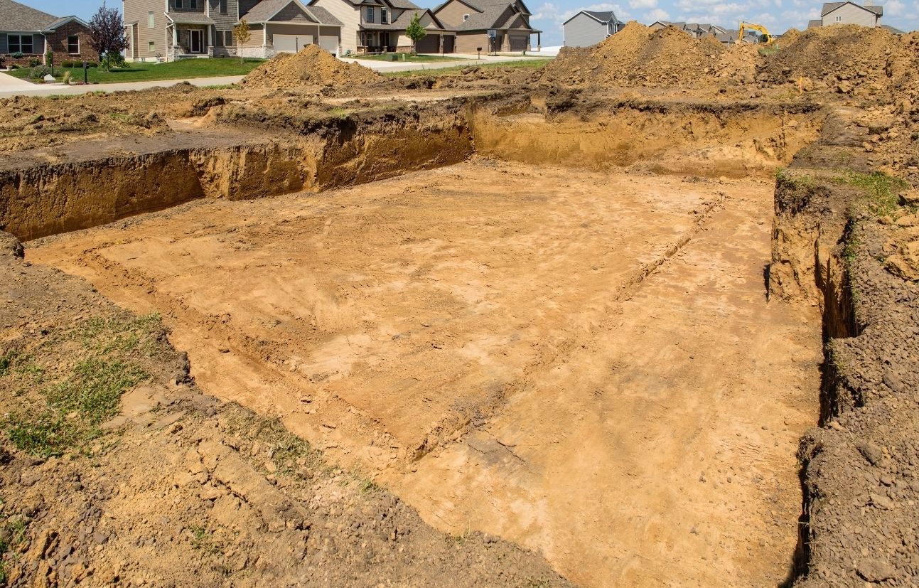 An excavated foundation pit with marked outlines in the dirt at a residential construction site.