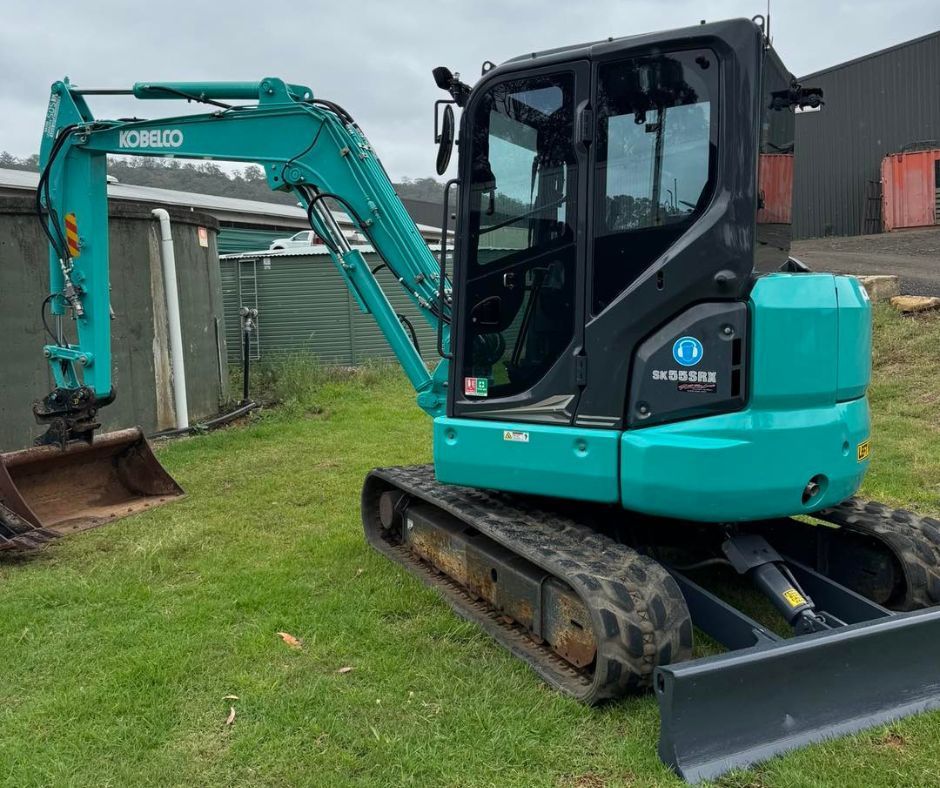 Teal excavator parked on grass beside a shed and warehouse Teal excavator parked on grass beside a shed and warehouse