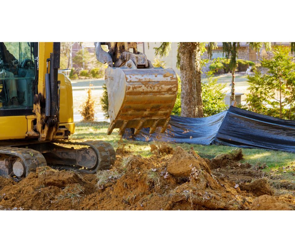 A yellow excavator sits in a grassy yard, its bucket positioned over a pile of freshly dug dirt near a blue tarp.