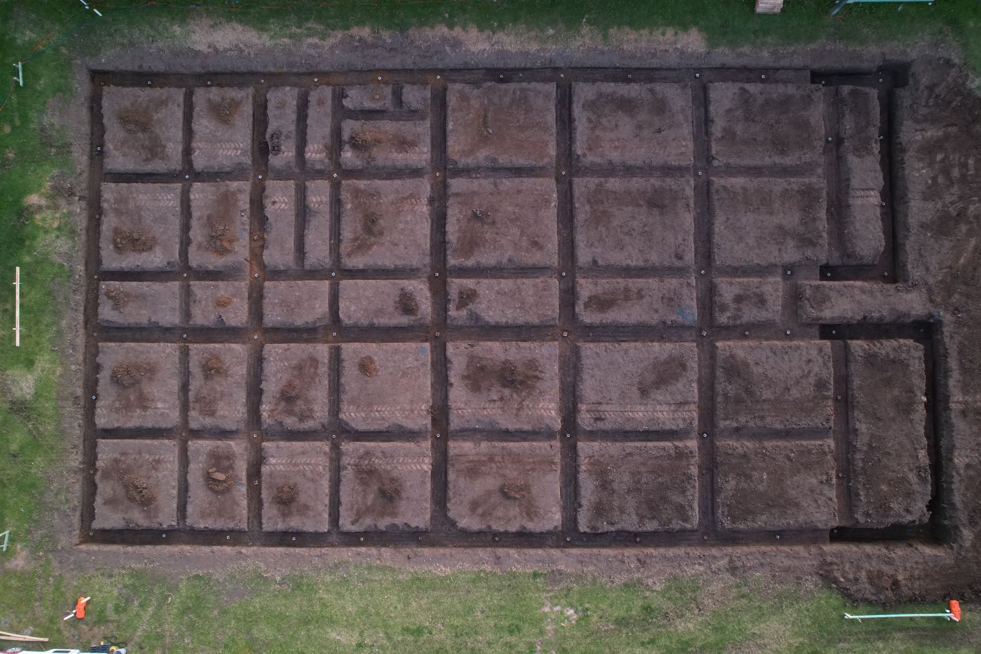 An aerial view of a rectangular excavation site in a grassy field, divided by trenches into a grid pattern.