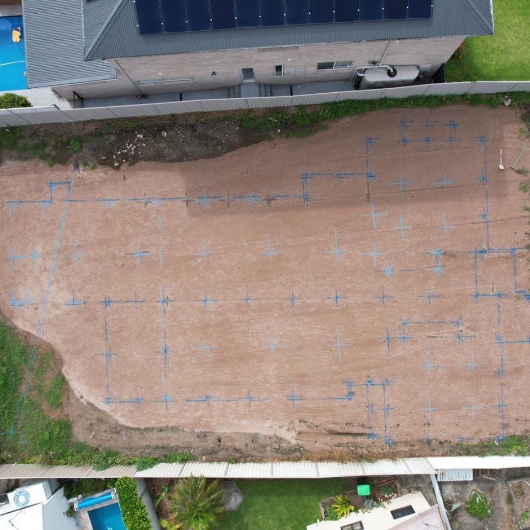 An aerial view of a construction site with blue survey markings on bare dirt, prepared for building a home foundation.