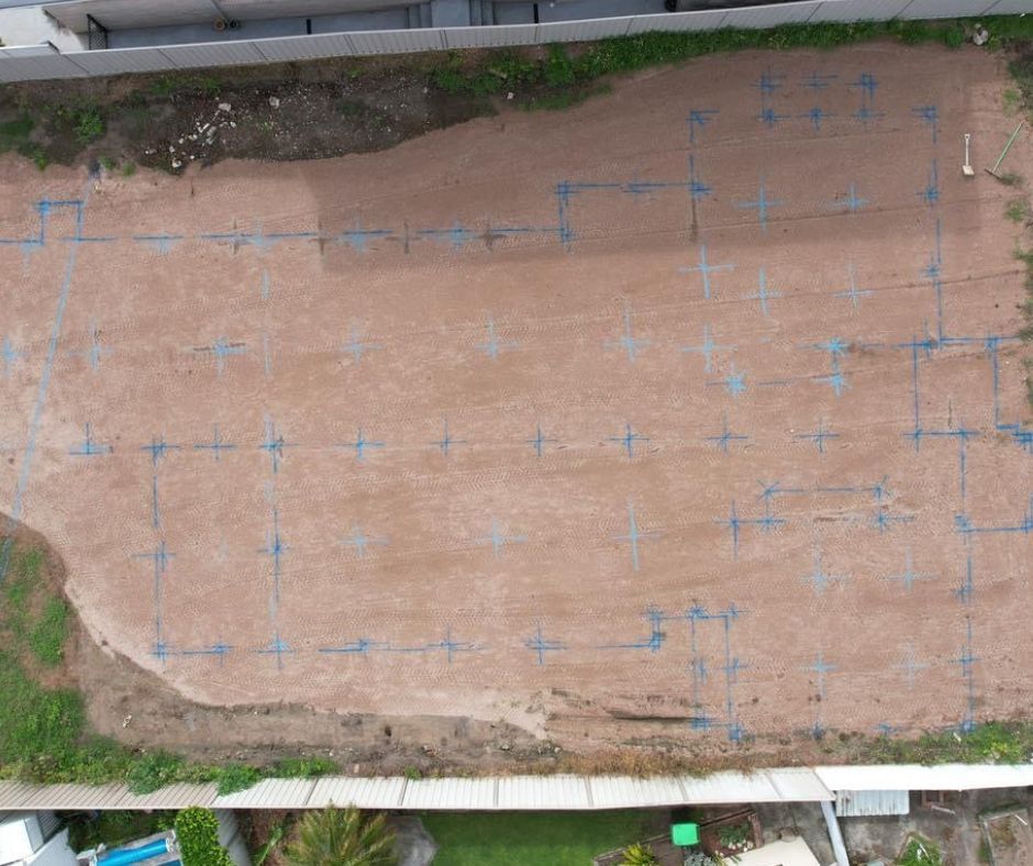 Aerial view of a vacant dirt lot marked with blue spray-painted foundation outlines for a future building construction.