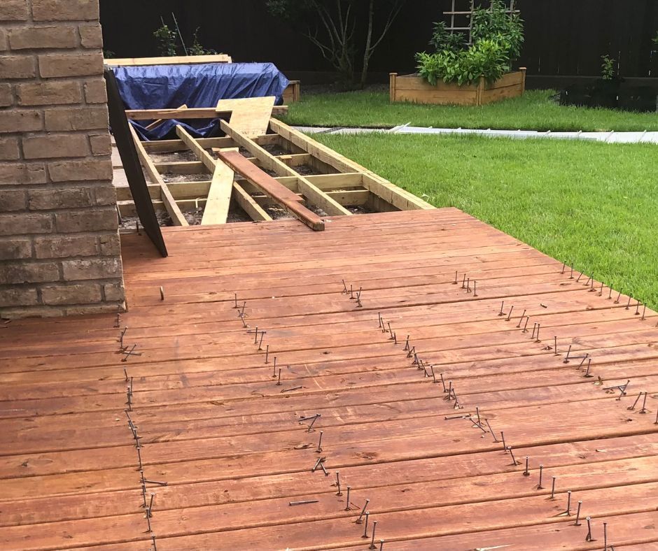 A backyard deck in the process of being built, showing a finished wooden section with exposed screws and an open frame.