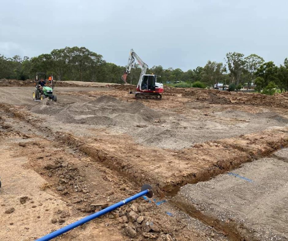 A small excavator works on a dirt construction site with trenches dug for a new building foundation.