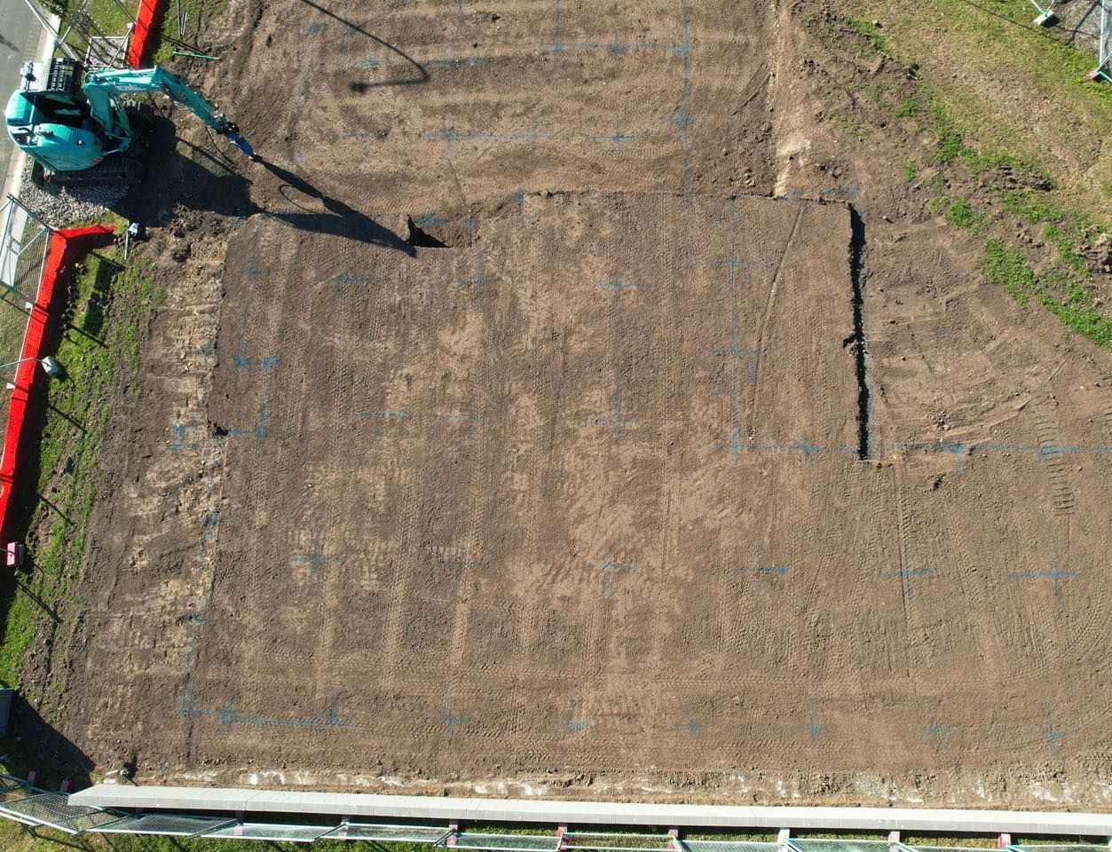 An aerial view of a backyard showing a large rectangular area marked with deep trenches for a residential foundation.