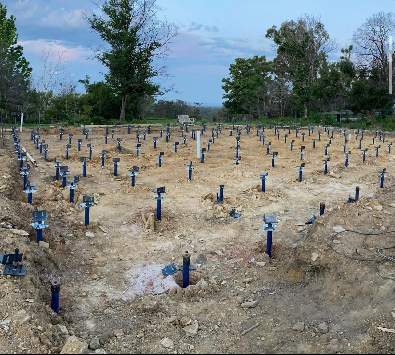 A grid of blue steel support piers installed in the dirt at a construction site before a building foundation is laid.