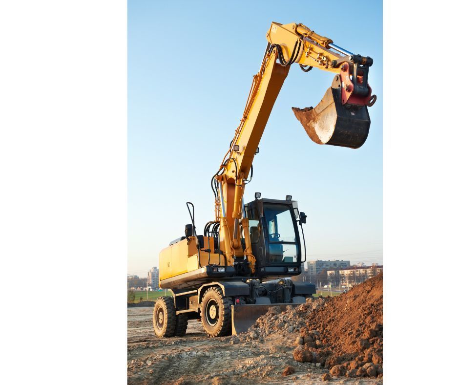 Yellow excavator on a construction site with its arm raised, set against a clear blue sky.