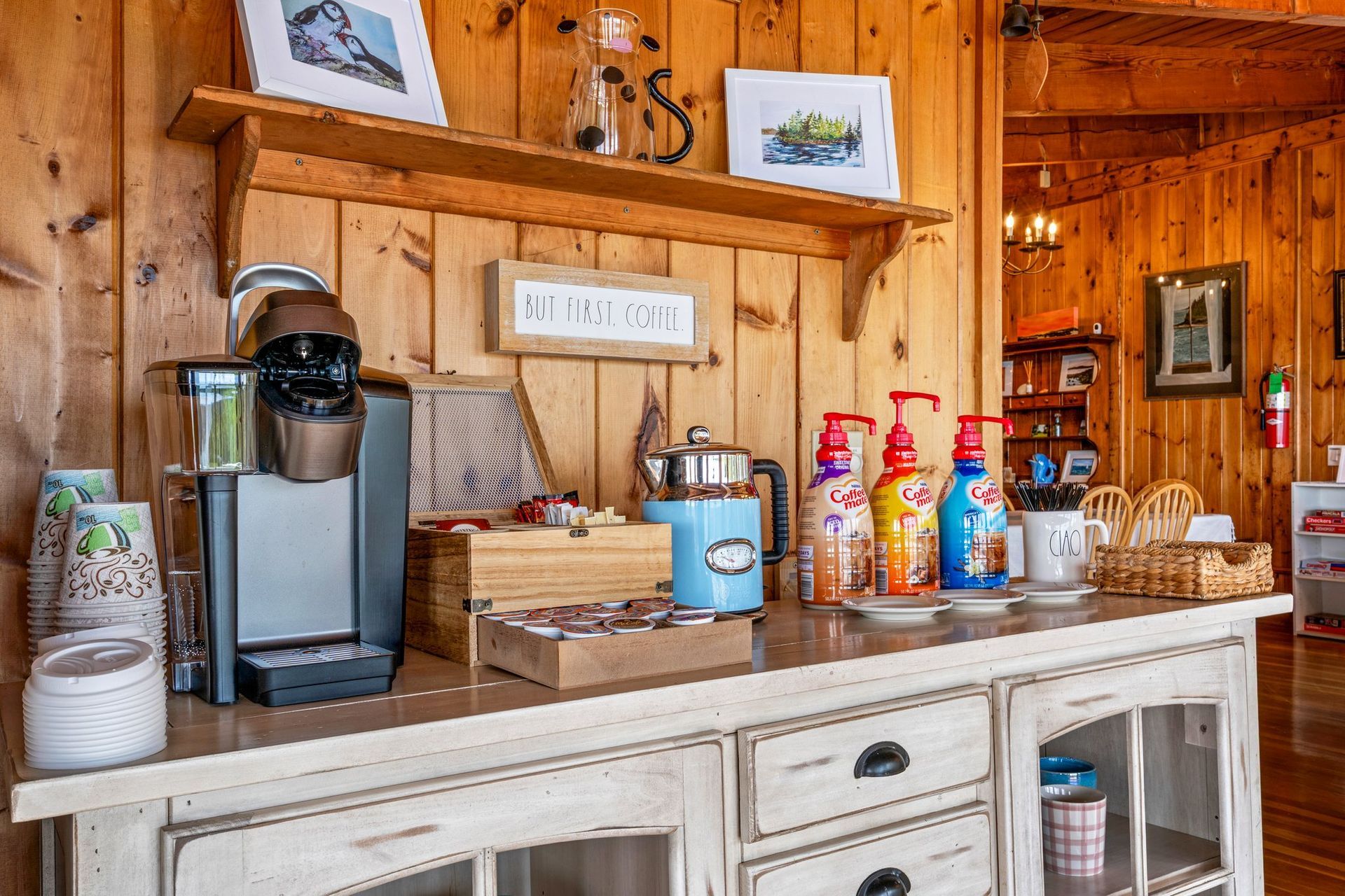 Coffee bar with espresso machine, mugs, and drink syrups on a white counter in a wood-paneled room
