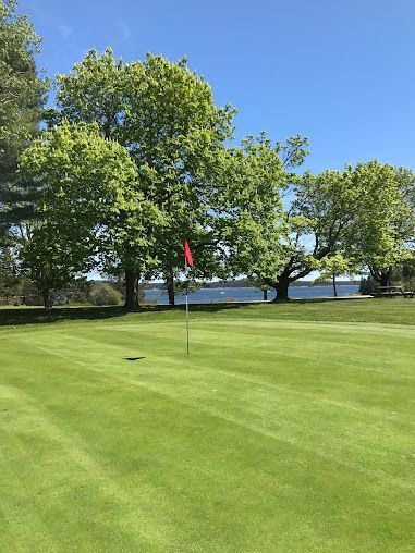 A golf course with trees and a lake in the background located near the Bluff House Inn.
