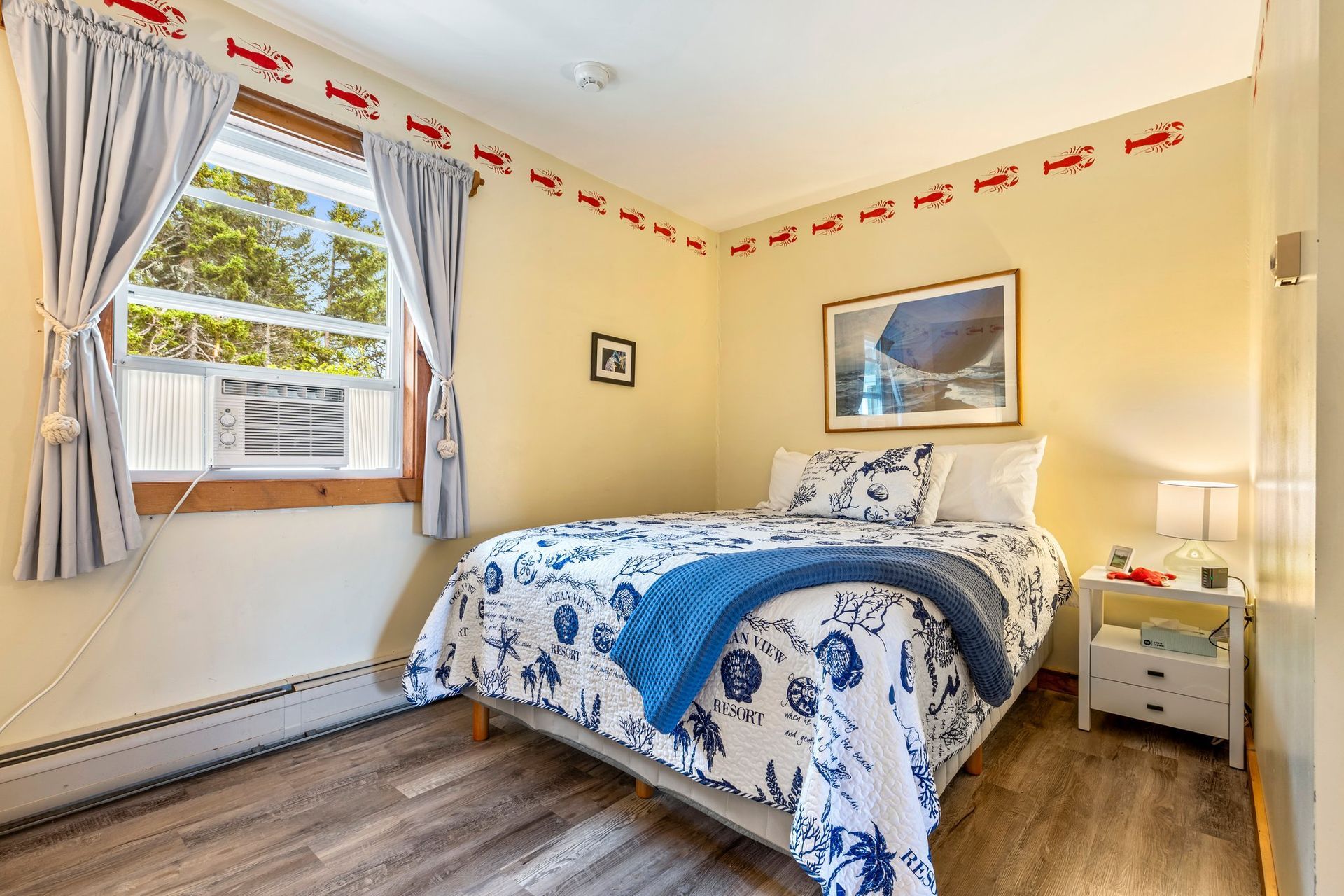 Bedroom with a bed, window, and lobster decor. The bed has blue and white patterned bedding. The walls are yellow.