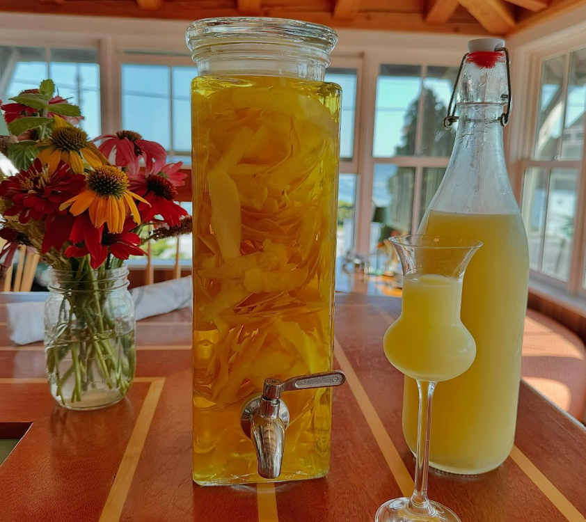 Two tall drinks on a wooden table with flowers in a vase, in a bright seaside dining room.